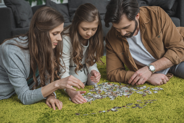 parents and daughter connecting puzzle pieces on floor in living room - Foto, Imagen