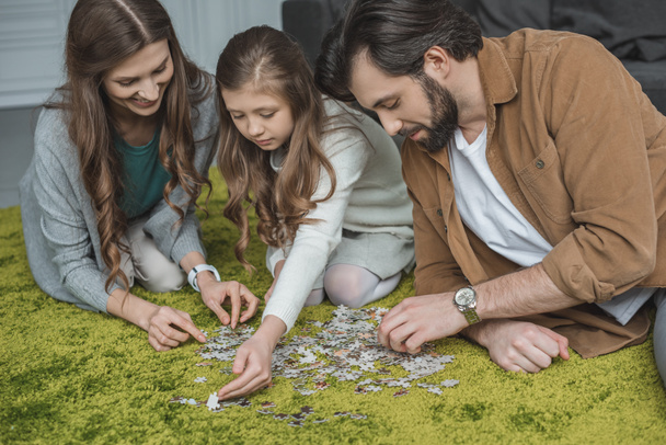 parents and daughter connecting puzzle pieces on carpet in living room - Fotó, kép