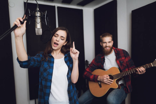 A girl and a guy sing a song to a guitar in a modern recording studio. The girl sings, and the guy plays the guitar. - Fotoğraf, Görsel