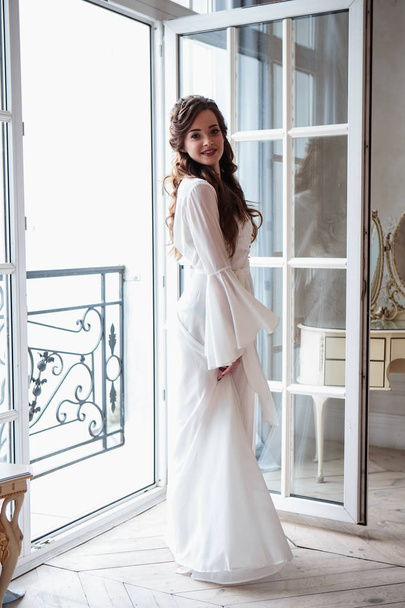 Beautiful bride in a white wedding peignoir in a morning. beauty portrait in interior - Photo, Image