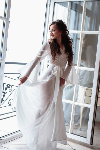 Beautiful bride in a white wedding peignoir in a morning. beauty portrait in interior - Фото, изображение