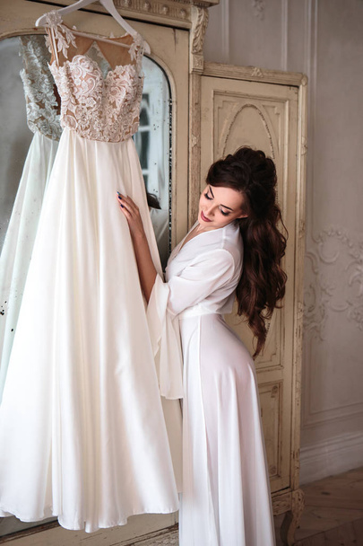 Beautiful bride in a white wedding peignoir in a morning. beauty portrait in interior - Фото, изображение