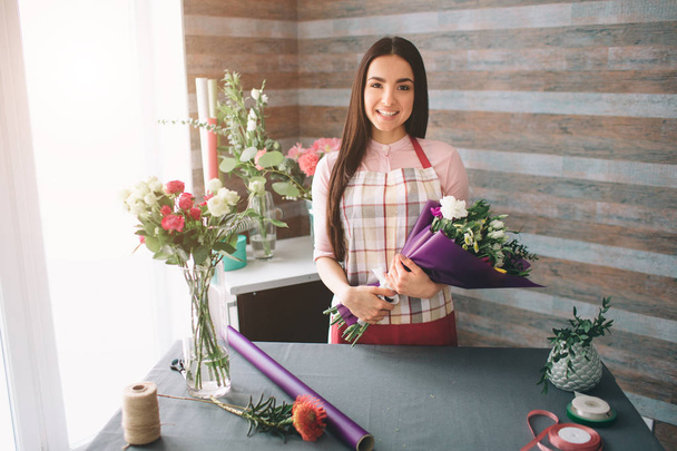 Female florist at work: pretty young dark-haired woman making fashion modern bouquet of different flowers. Women working with flowers in workshop - 写真・画像