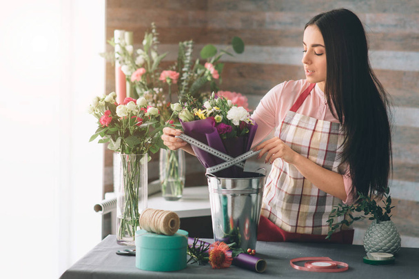 Female florist at work: pretty young dark-haired woman making fashion modern bouquet of different flowers. Women working with flowers in workshop - Photo, image