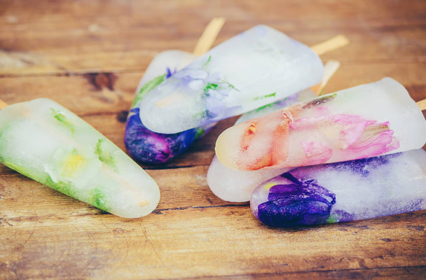 frozen flowers in ice cubes and ice cream on a stick. selective focus. - Photo, Image