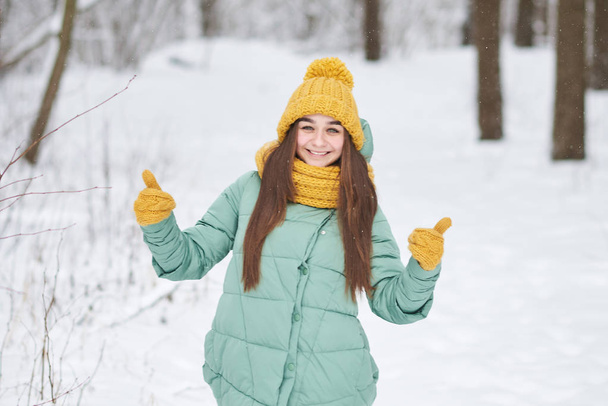 Belle jeune fille en bonnet tricoté montre "classe" en mitaines, sur fond de forêt d'hiver
 - Photo, image