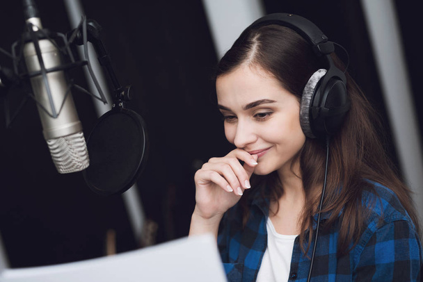 The girl in the recording studio sings a song. Her headphones are on her head. Next to her is a microphone. She emotionally sings the song. - Foto, Imagem