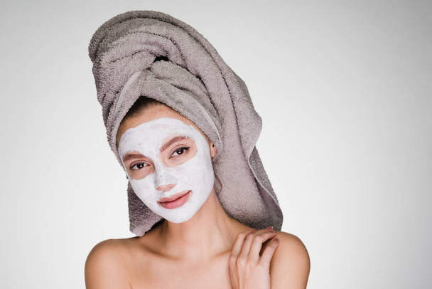 a cute young girl with a towel on her head applied a white nutritious mask on her face, a spa procedure - Фото, зображення