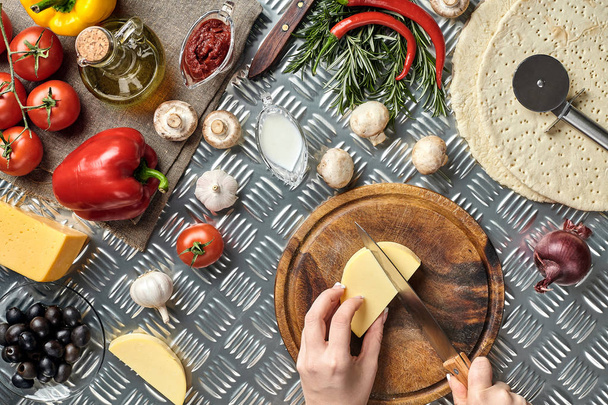 részleges kilátás nyílik a nő vágás sajtot, házi készítésű olasz pizza főzés közben - Fotó, kép
