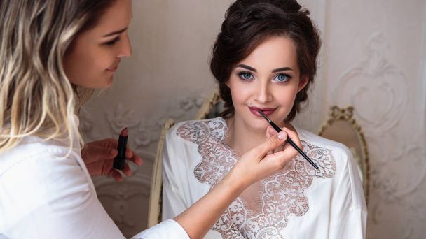makeup artist preparing beautiful bride before the wedding in a morning - Photo, image