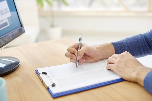 Close-up of businessmans hand writing something on the paper. Casual professional man sitting at desk and fill the form.  - Photo, Image