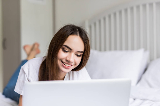 Hymyilevä nainen kiinni hänen sosiaalisen median hän rentoutuu sängyssä kannettavan tietokoneen laiska päivä
 - Valokuva, kuva