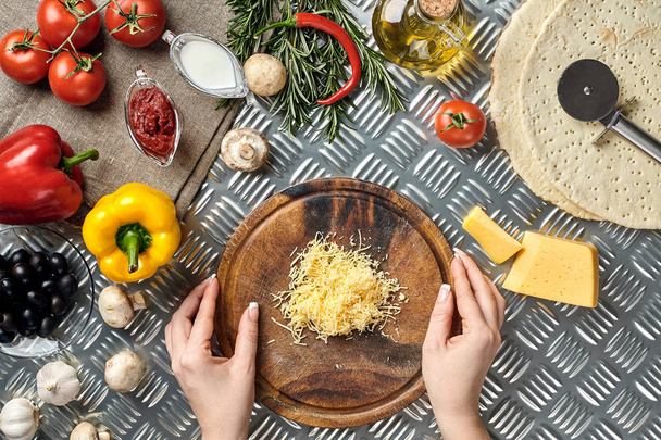Γυναικεία χέρια τρίβονται τυρί τριμμένο για πίτσα, συστατικά για το μαγείρεμα πίτσα σε μεταλλικό πίνακα, το top view - Φωτογραφία, εικόνα