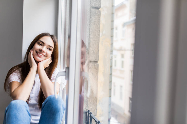 Kaunis hymyilevä nainen istuu ikkunalaudalla
 - Valokuva, kuva