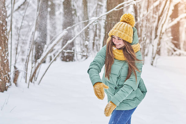 Beautiful young girl in a knitted hat,playing in the snow in forest - Photo, Image