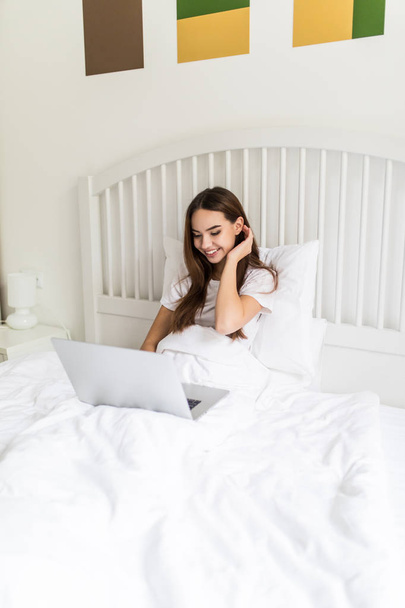 Молода жінка використовує ноутбук у спальні. Жіноча модель на ліжку, що працює на ноутбуці
. - Фото, зображення