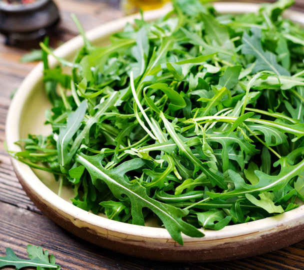 Fresh leaves of arugula in a bowl on a  wooden background - Photo, Image