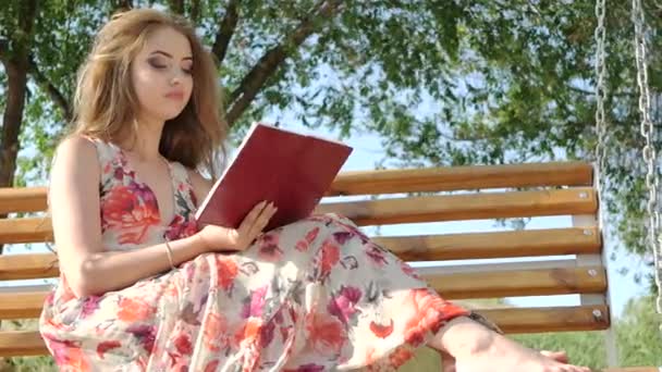 Girl with a book on a bench in the park - Кадры, видео