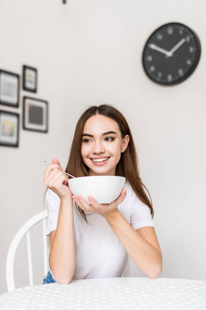 Portrait of beautiful young woman having breakfast in the kitchen in the morning - Foto, imagen