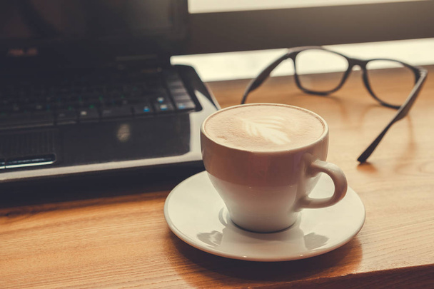 Rövid idő használ egy laptop a kávézóban kávét iszik. Csésze kávé szemüveg és a laptop az ablak betűtípusa - Fotó, kép
