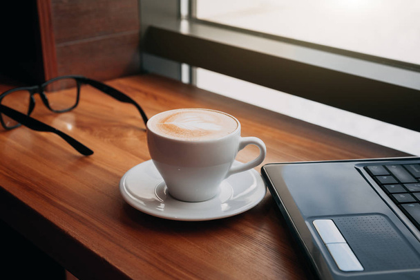 Pití kávy při používání notebooku v kavárně. Šálek kávy s brýlemi a notebooku v písmu okna - Fotografie, Obrázek