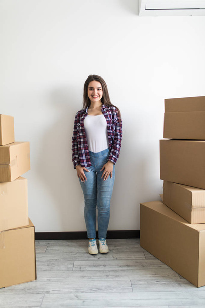 Attractive young woman is moving, standing among cardboard boxes, smiling - Foto, Bild