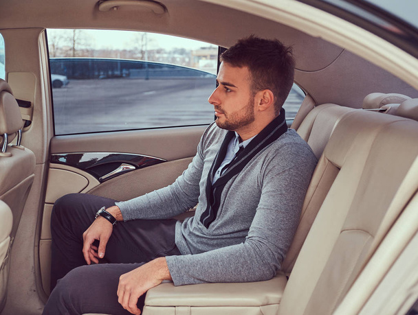A handsome fashionable male in elegant clothing sitting in the car. - Foto, imagen