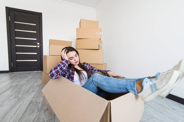 Cheerful sad and tired woman sitting in a cardboard box white moving in new appartmant - Foto, Imagen