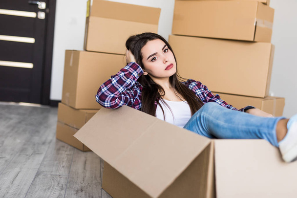 Fiatal nő ül benne egy doboz egy rakás költöztető dobozok között fáradt - Fotó, kép