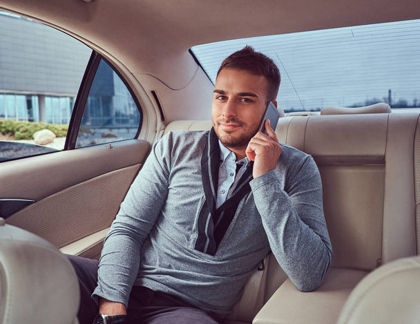 Um empresário bonito em roupas elegantes trabalhando, falando ao telefone enquanto sentado no carro
. - Foto, Imagem