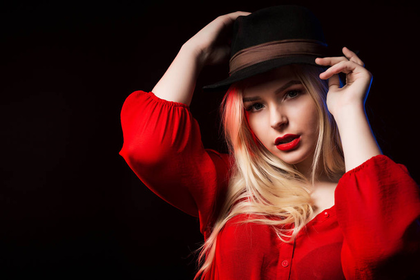 Очаровательная молодая женщина в красной блузке и коричневой шляпе позирует на studi
 - Фото, изображение