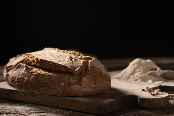 Pane appena sfornato su tavolo di legno su sfondo scuro
 - Foto, immagini