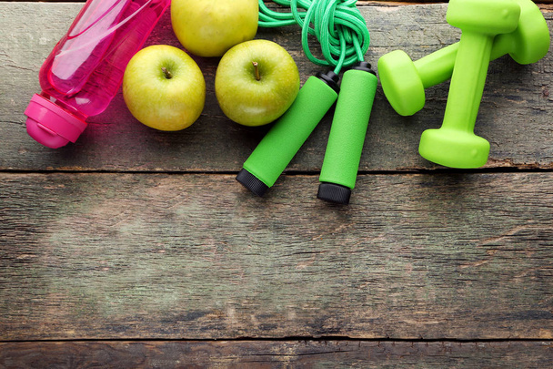 Green apple, skipping rope, pink bottle and dumbbells on wooden table - Photo, Image