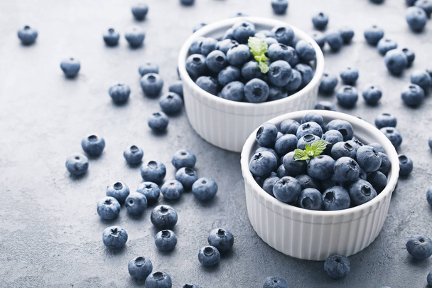 Ripe blueberries in bowls on grey wooden table - Foto, Imagen
