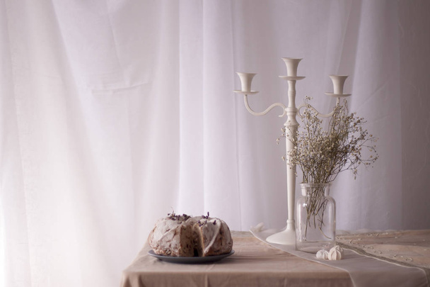 Paistettu kotitekoinen kakku kukkia maljakko ja kattokruunu pöydällä
 - Valokuva, kuva