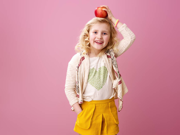Pink mood. smiling modern child with wavy blonde hair on pink background holding an apple on head - Photo, Image