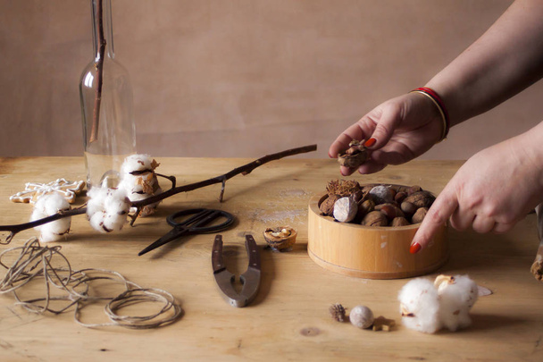 Primer plano de manos femeninas pelando nueces sobre mesa de madera con rama
 - Foto, Imagen