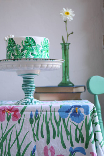 Holiday kakku palmunlehtiä suunnittelu. Trooppinen syntymäpäiväjuhla inspiraatiota. Maukas kakku vohveli paperi monstera lehdet pöydälle vanhoja kirjoja ja kukka maljakko
  - Valokuva, kuva