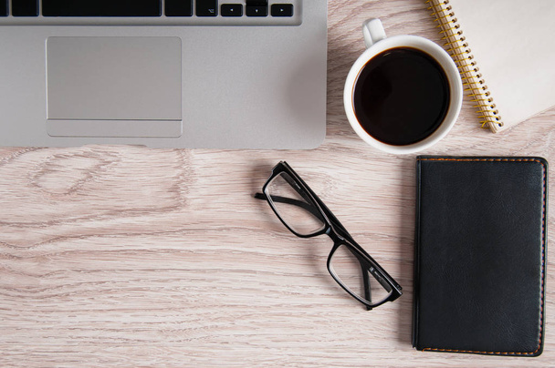 Вид сверху ноутбука и блокнота с очками и карманником на деревянном рабочем столе и чашкой кофе
. - Фото, изображение