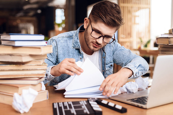 Freelancer man reviewing notes sitting at desk surrounded by books. - Photo, Image