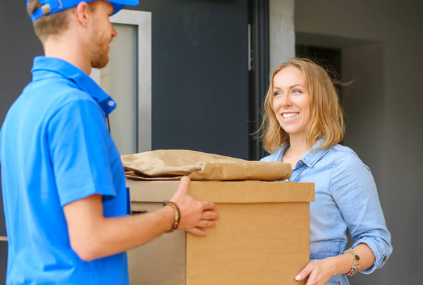 Smiling delivery man in blue uniform delivering parcel box to recipient - courier service concept. Smiling delivery man in blue uniform - Foto, Imagem