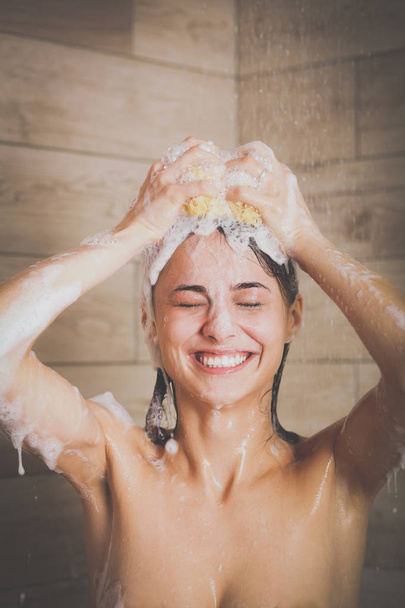 Young beautyful woman under shower in bathroom. - Фото, изображение