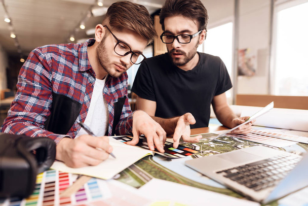 Deux hommes pigistes en chemise et t-shirt regardant des échantillons de couleur à l'ordinateur portable au bureau
. - Photo, image