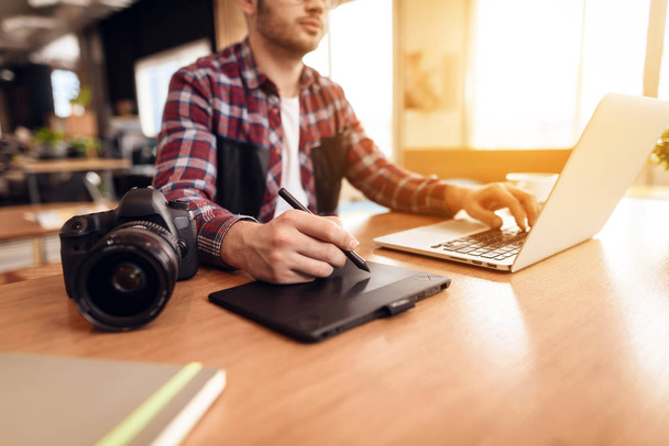 Freelancer man typing and drawing at laptop sitting at desk. - Fotó, kép