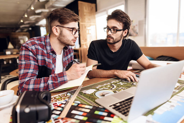 Two freelancer men in shirt and t-shirt taking notes at laptop at desk. - Fotoğraf, Görsel