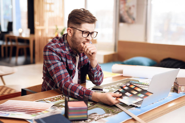 Freelancer hombre en camisa mirando muestras de color en el portátil sentado en el escritorio
. - Foto, imagen