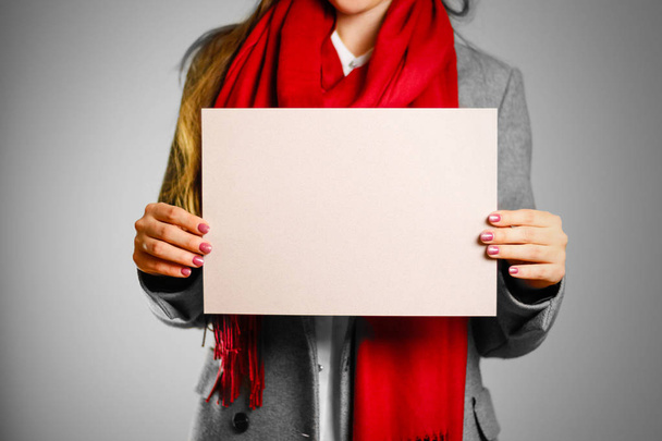 A girl in grey coat and red scarf keeps a beige clean blank shee - Фото, зображення
