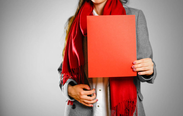 Una chica con abrigo gris y bufanda roja mantiene una sábana en blanco limpia y roja
  - Foto, Imagen