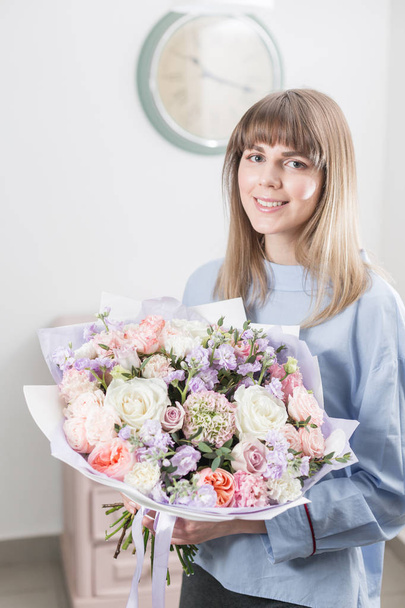 Sunny spring morning. Young happy woman holding a beautiful luxury bouquet of mixed flowers. the work of the florist at a flower shop. vertical photo - Zdjęcie, obraz
