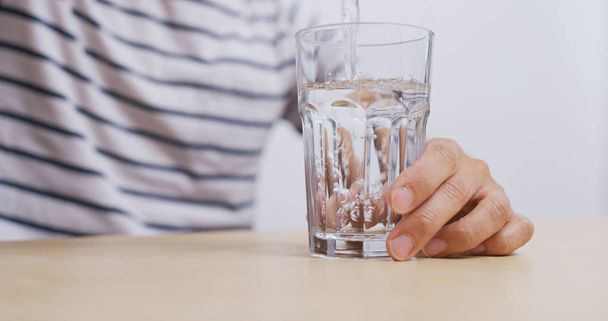 Man giet water in glas - Foto, afbeelding